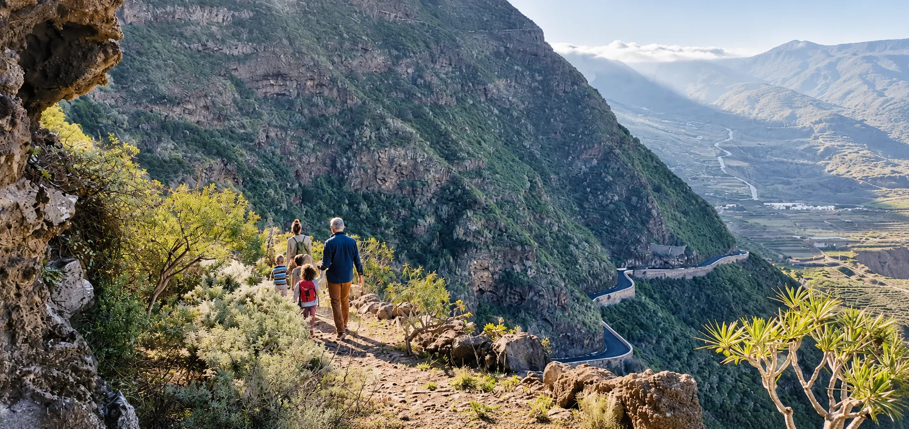 Familie auf einem Wanderweg am Berghang, unten die Serpentinenstraße und das Tal